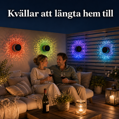 Mysig kvällsstämning på en altan där ett par sitter i en soffa och dricker vin. I bakgrunden lyser flera solarcellslampor i metall med vackra, färgstarka mandalamönster på väggen.